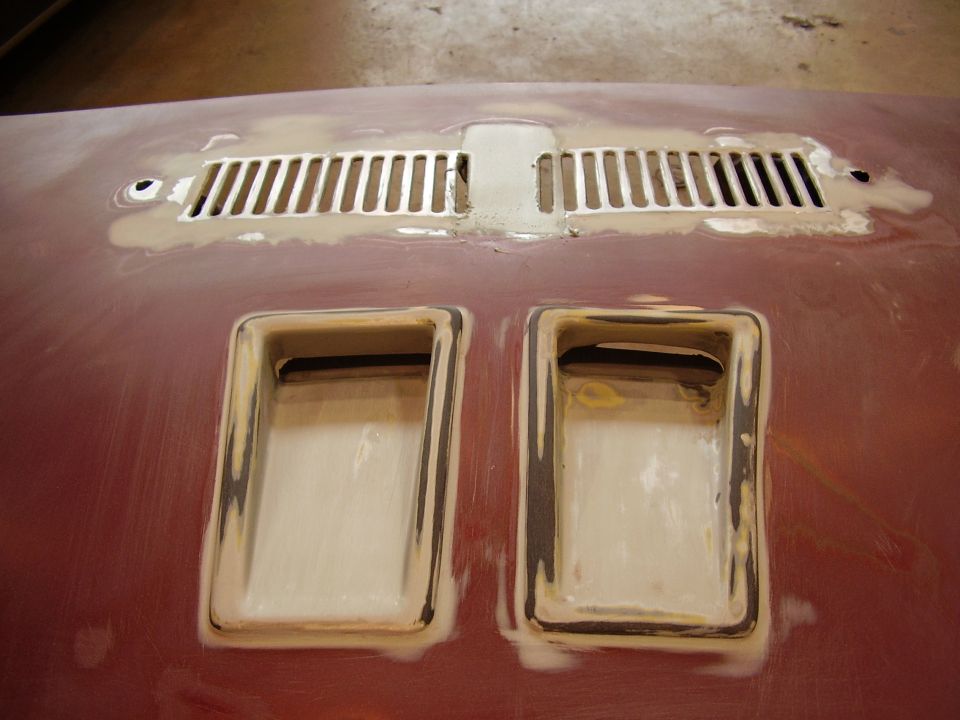 Red car hood with two rectangular scoops and a central vent grille, undergoing bodywork