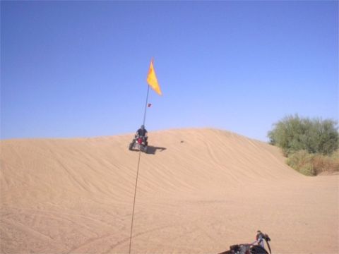1993 Ford Bronco - An ATV rides up a sand dune under a clear blue sky, with a yellow flag attached to a pole.
