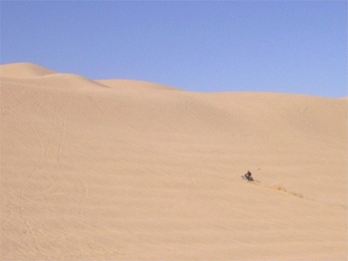 ATV kicking up dust on a sand dune under a clear blue sky