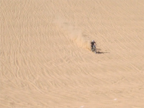 Motorcycle kicking up dust on a sand dune
