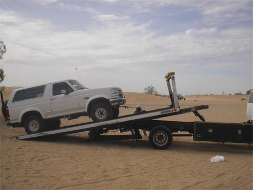 White 1993 Ford Bronco being towed on a flatbed truck in a desert landscape