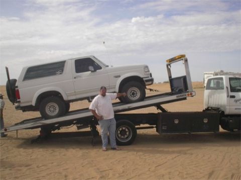 1993 Ford Bronco - A white 1993 Ford Bronco is being towed on a flatbed truck in a sandy area.