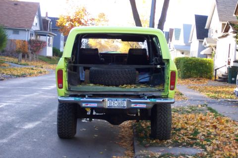 1978 Ford Bronco - Rear view of a lime green 1978 Ford Bronco, showing the spare tire and open cargo area on a street lined with houses.