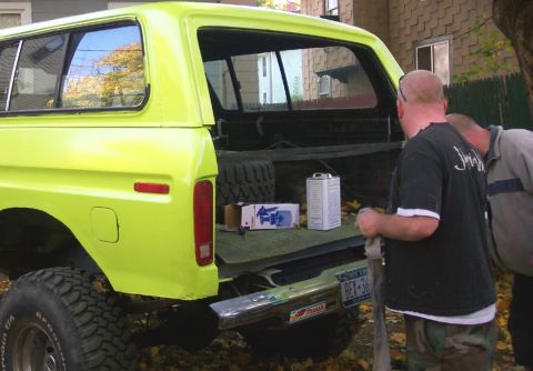 1978 Ford Bronco - The rear of a bright yellow 1978 Ford Bronco is shown with its tailgate down, revealing a spare tire and various containers.