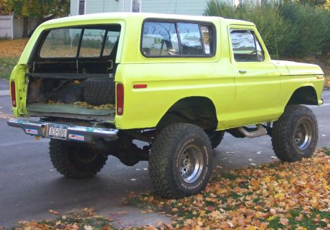 1978 Ford Bronco - A lifted 1978 Ford Bronco in yellow is viewed from the rear, showing its off-road tires and open tailgate.