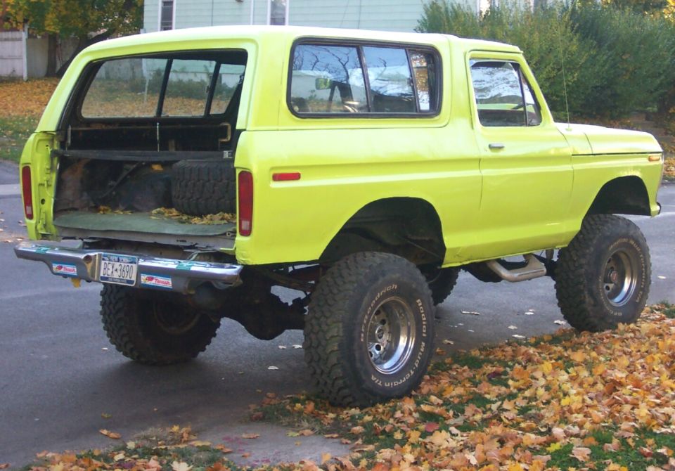 Yellow 1978 Ford Bronco with lifted suspension and off-road tires, rear view with tailgate down
