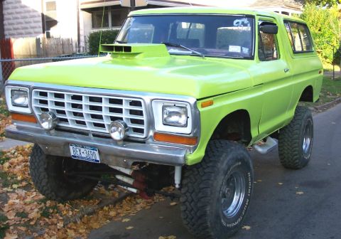 1978 Ford Bronco - This lifted SUV, possibly a 1978 Ford Bronco, is parked on a street with fallen leaves on the ground.