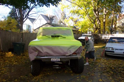 1978 Ford Bronco - A man works on a vehicle covered in protective plastic sheeting in a yard with fallen leaves.