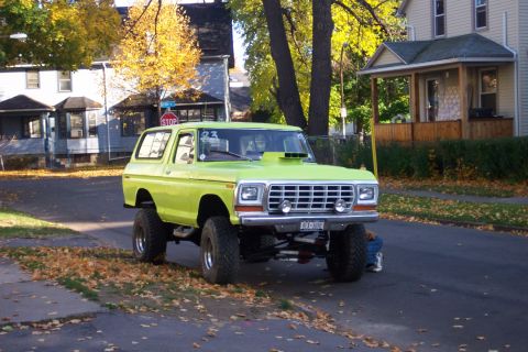 1978 Ford Bronco - This modified SUV features a prominent hood scoop and sits high on lifted suspension, with a person attending to its underside.