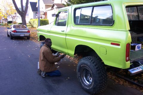 1978 Ford Bronco - A person works on the underside of a vintage truck parked on a residential street.