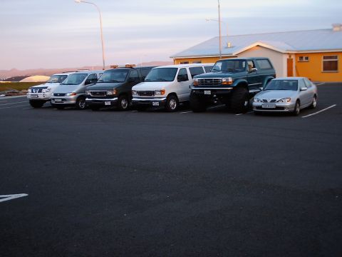 1996 Ford Bronco - Several vehicles are parked in a lot, including a lifted green truck with large tires.