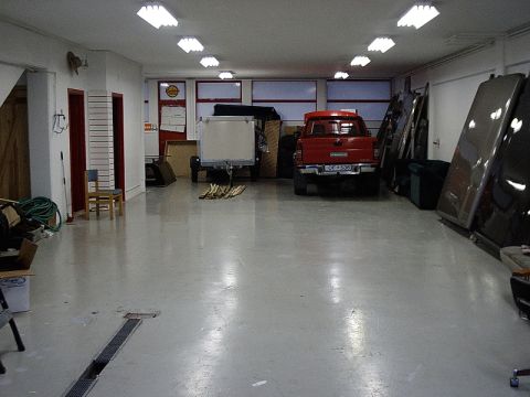 1996 Ford Bronco - A red pickup truck is parked inside a garage with a trailer and other items.