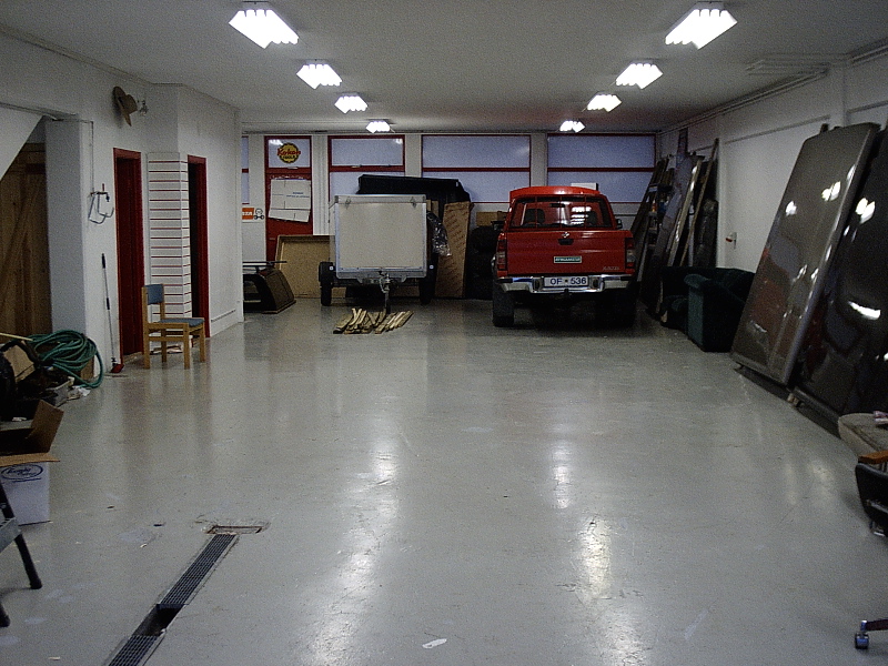 Red pickup truck parked rear-facing inside a garage next to a white trailer