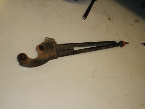 1996 Ford Bronco - This is a photograph of a single, rusty metal automotive part, likely a linkage or bracket, lying on a light-colored surface.