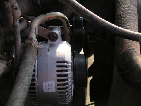 1994 Ford Bronco - Freshly installed silver alternator in an engine bay, still wearing a parts label reading '20-228-10-2 / 12V 130A', showing its finned case…