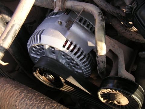 1994 Ford Bronco - Close-up of a newly installed cast-aluminum alternator in a dusty engine bay, with copper windings visible through the vented case and a se…
