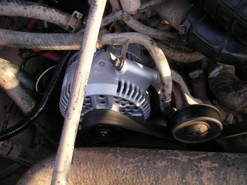 1994 Ford Bronco - Wider engine-bay view of a new silver alternator bolted in place with the serpentine belt routed over its pulley and a smooth idler pulley…