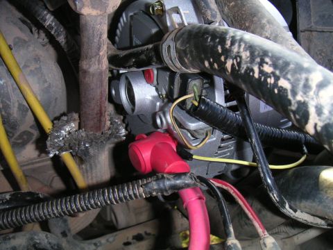 1994 Ford Bronco - Tight shot of a freshly installed silver alternator in a dusty engine bay, with a heavy red battery cable in a red insulating boot bolted t…