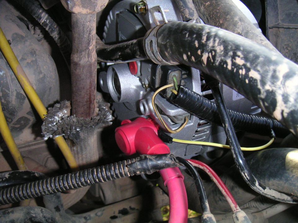 New silver alternator with red battery cable and boot installed in a dirty engine bay