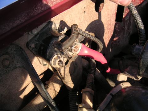 1994 Ford Bronco - Close-up of a dusty engine bay showing the starter solenoid mounted on the inner fender, with a red battery cable in a pink insulating boot…
