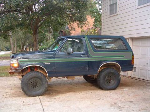 1993 Ford Bronco - Side view of a dark blue Ford Bronco with aftermarket wheels and visible front fender damage.