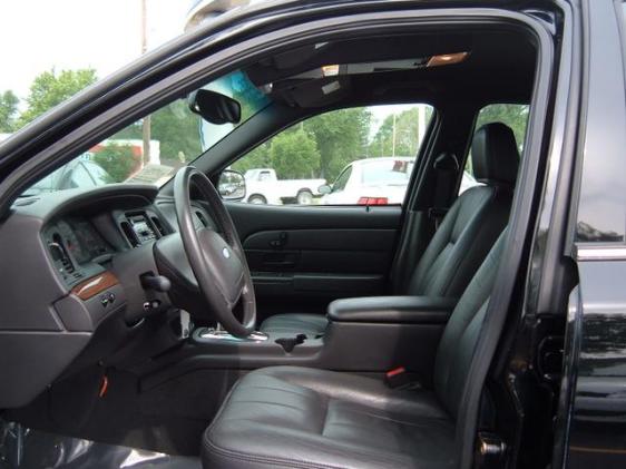 Black leather driver's seat, Ford steering wheel and wood-trim dash seen through open door of black sedan