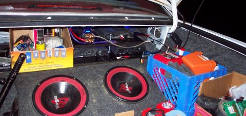 1985 Ford LTD Crown Victoria - The trunk of a car is filled with audio equipment and various items, including two subwoofers and a blue crate.
