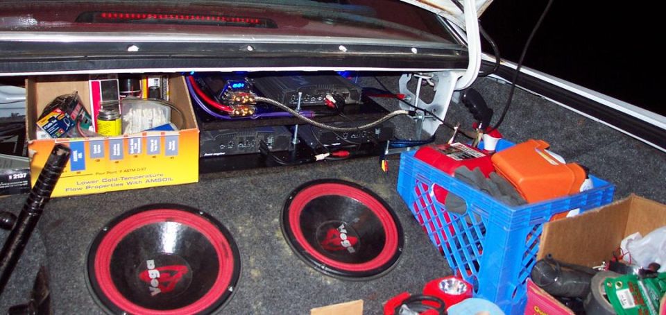 Car trunk with two subwoofers, amplifiers, and a blue crate of supplies