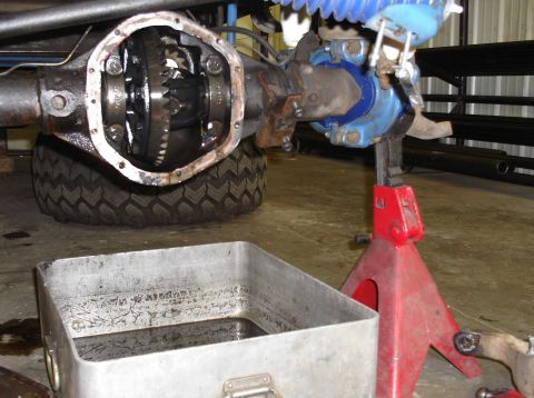 1979 Ford Bronco - Close-up of a vehicle's differential with the cover removed, resting on a jack stand with a drain pan nearby.