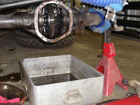 1979 Ford Bronco - Differential housing gears exposed during maintenance, with an oil drain pan and jack stand visible.