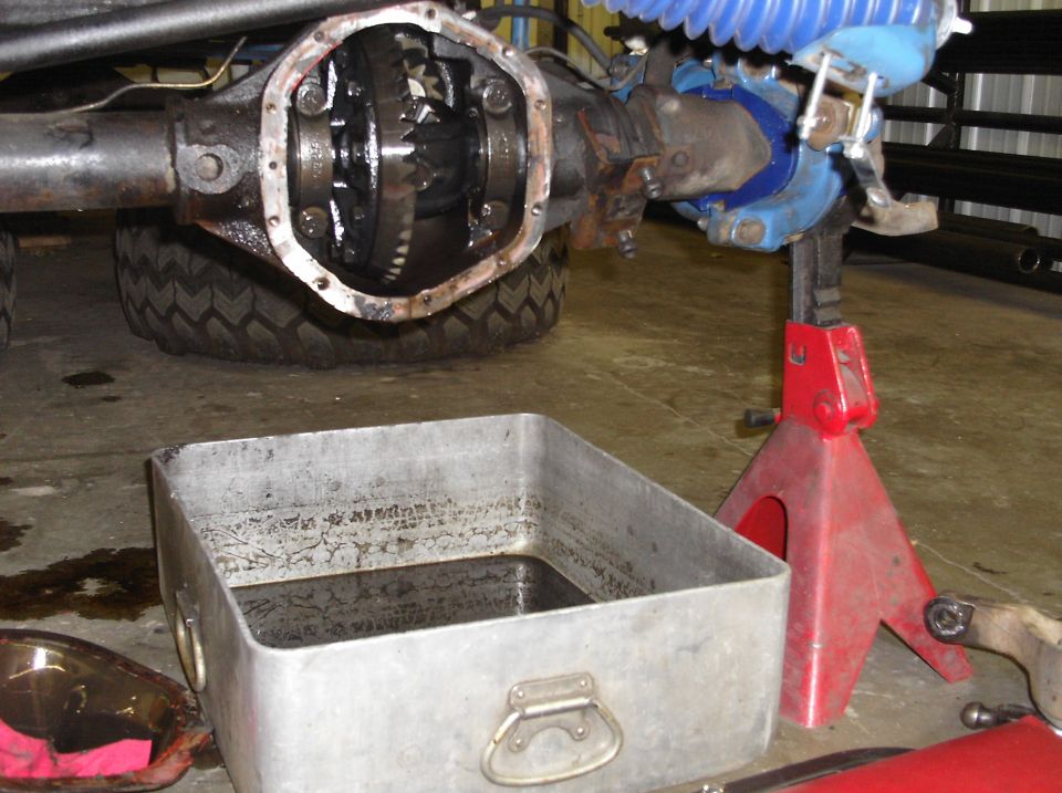 Differential housing with gears exposed, oil drain pan nearby, vehicle on jack stand