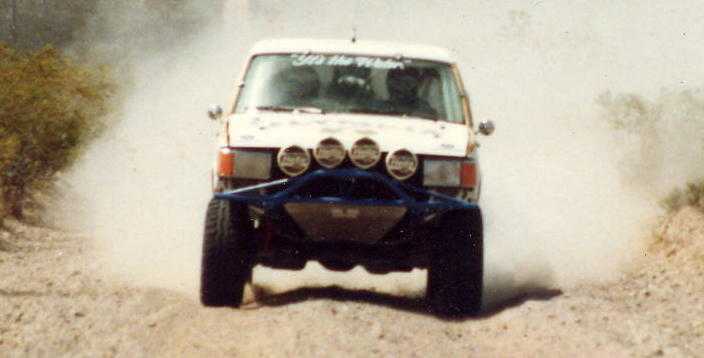 White off-road race truck jumping on a dusty desert trail, front view