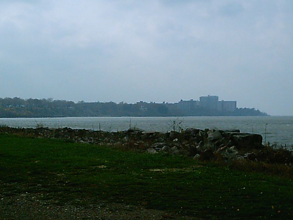 Waterfront buildings across a body of water, with rocks and grass in the foreground
