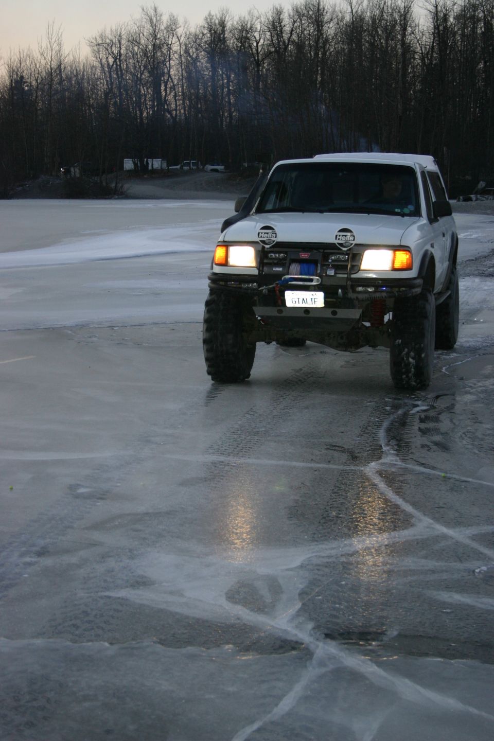 White SUV with large tires driving on a cracked ice surface. Lights are on
