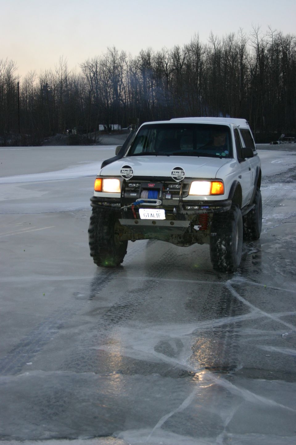 White SUV with large tires on ice, front view. Aftermarket bumper with Hella lights and winch