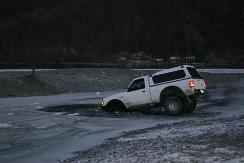 2003 Jeep TJ - A white pickup truck is stuck in icy water, with its front wheels submerged and the rear tires struggling for traction.