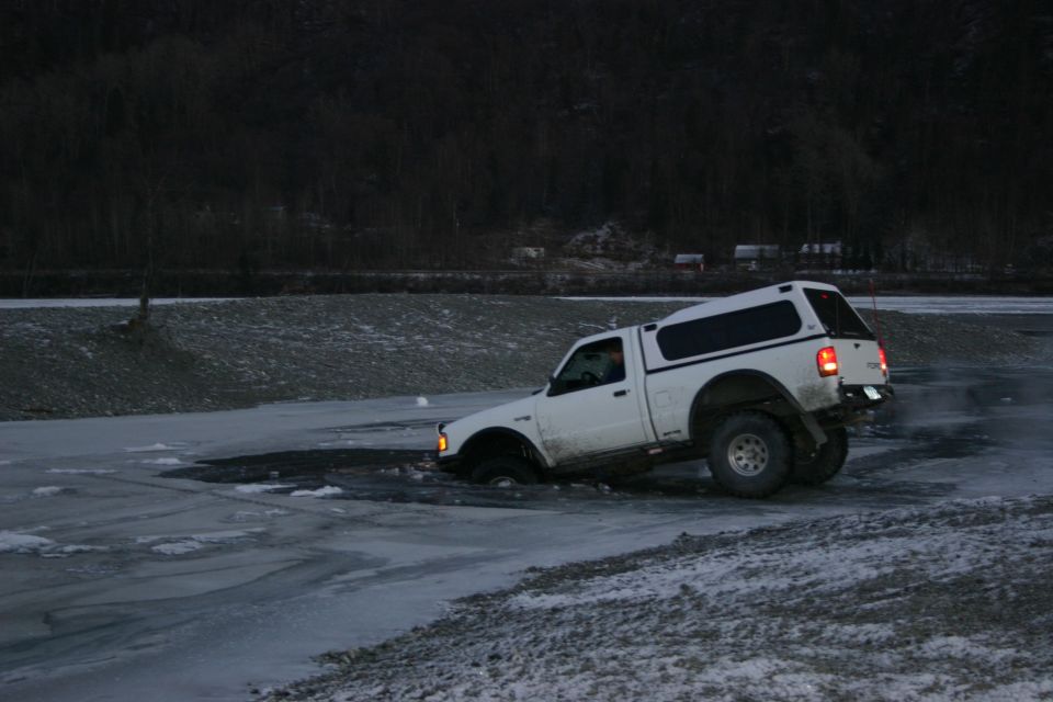 White pickup truck with a camper shell stuck in icy water, viewed from the front-three-quarter angle