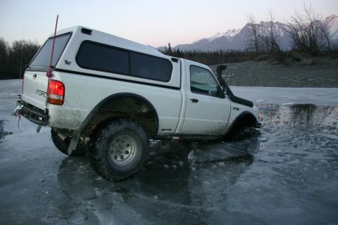 2003 Jeep TJ - A white Ford Ranger pickup truck is stuck in icy water with mountains in the background.