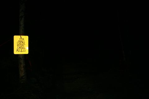 2003 Jeep TJ - A yellow sign indicating "Jim Creek Trail Access" is illuminated at night, attached to a pole in a dark, outdoor setting.