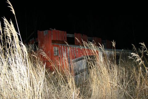 2003 Jeep TJ - An old, weathered red building stands abandoned amidst tall, dry grass under a dark night sky.