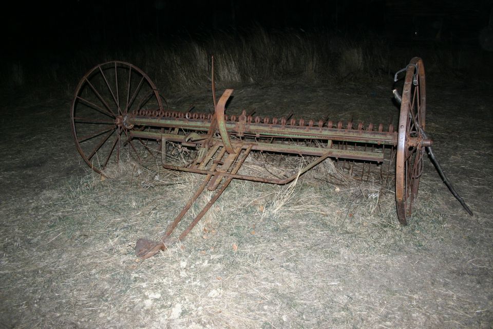 Rusty farm equipment with large spoked wheels and cutting bar