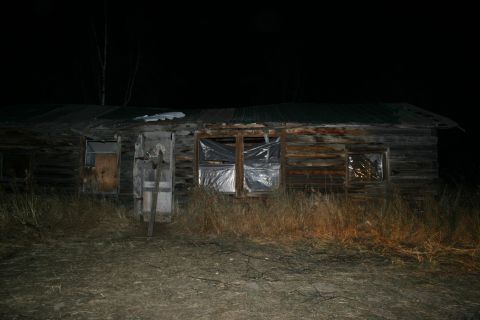 2003 Jeep TJ - An old, weathered cabin stands in darkness, its windows covered with plastic and wood.
