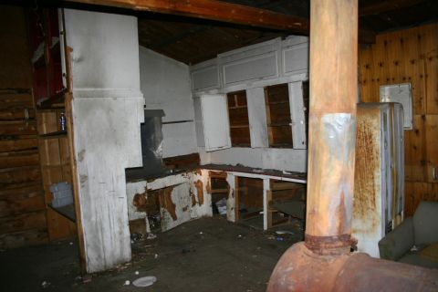 2003 Jeep TJ - The interior of a room shows signs of severe neglect and disrepair, with damaged cabinetry and a prominent rusty stovepipe.