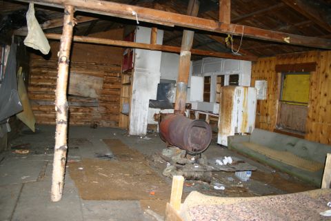 2003 Jeep TJ - The interior of a rustic cabin features a wood stove, a sofa, and a refrigerator.