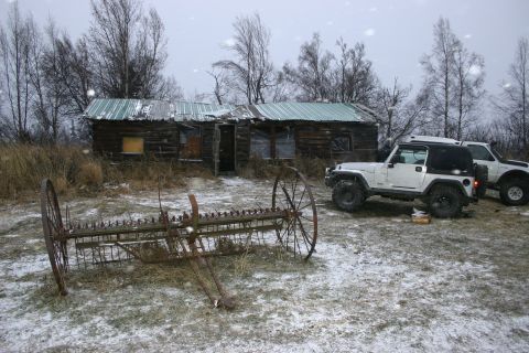 2003 Jeep TJ - Two Jeeps and an old farm rake sit outside a weathered cabin during a snowfall.