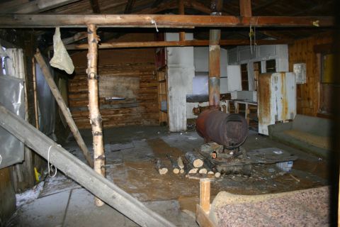2003 Jeep TJ - The interior of a rustic cabin shows a wood-burning stove, basic kitchen facilities, and seating areas.
