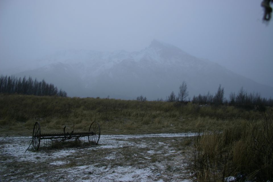 old farm rake in a field with a snowy mountain in the background under a hazy sky