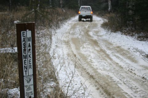 2003 Jeep TJ - Pickup truck travels down a snowy trail past an easement marker sign.