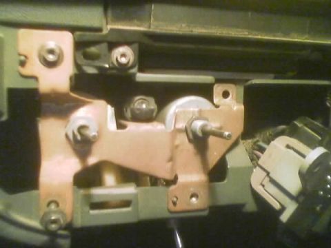 1990 Ford Bronco - Detailed view of a copper-toned mounting bracket with metal shafts and connectors, part of a dashboard switch assembly.