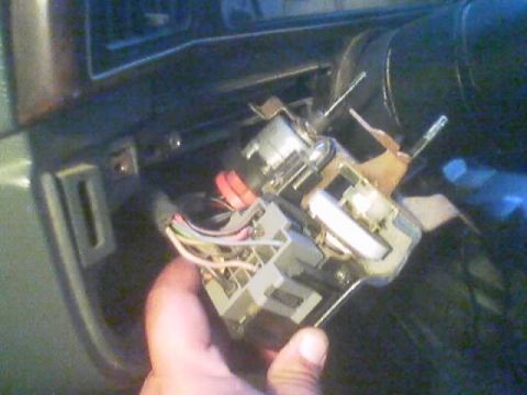 1990 Ford Bronco - hand holds a removed electrical switch assembly with a colorful wiring harness in front of a vehicle dashboard and door panel.